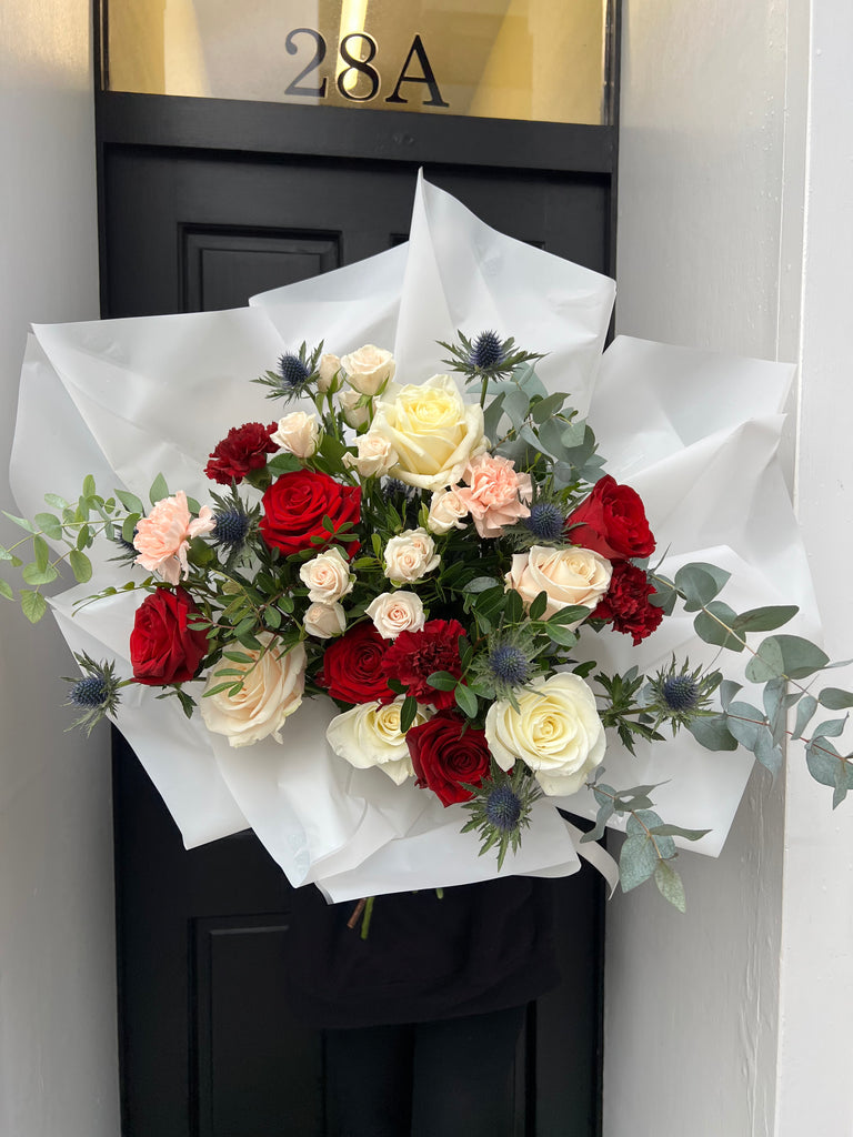 Gorgeous bouquet with red naomi roses, white avalanche roses, blue thistle, peach spray roses, pink carnations and eucalyptus. 