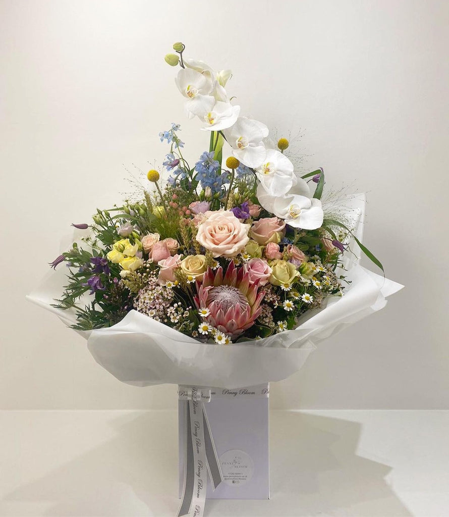 white bouquet with fresh spring flowers including orchids, bluebells, roses, protea, daisies, was flower and thistle.