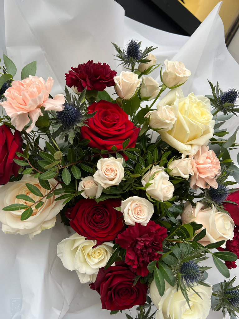 Gorgeous bouquet with red naomi roses, white avalanche roses, blue thistle, peach spray roses, pink carnations and eucalyptus. 