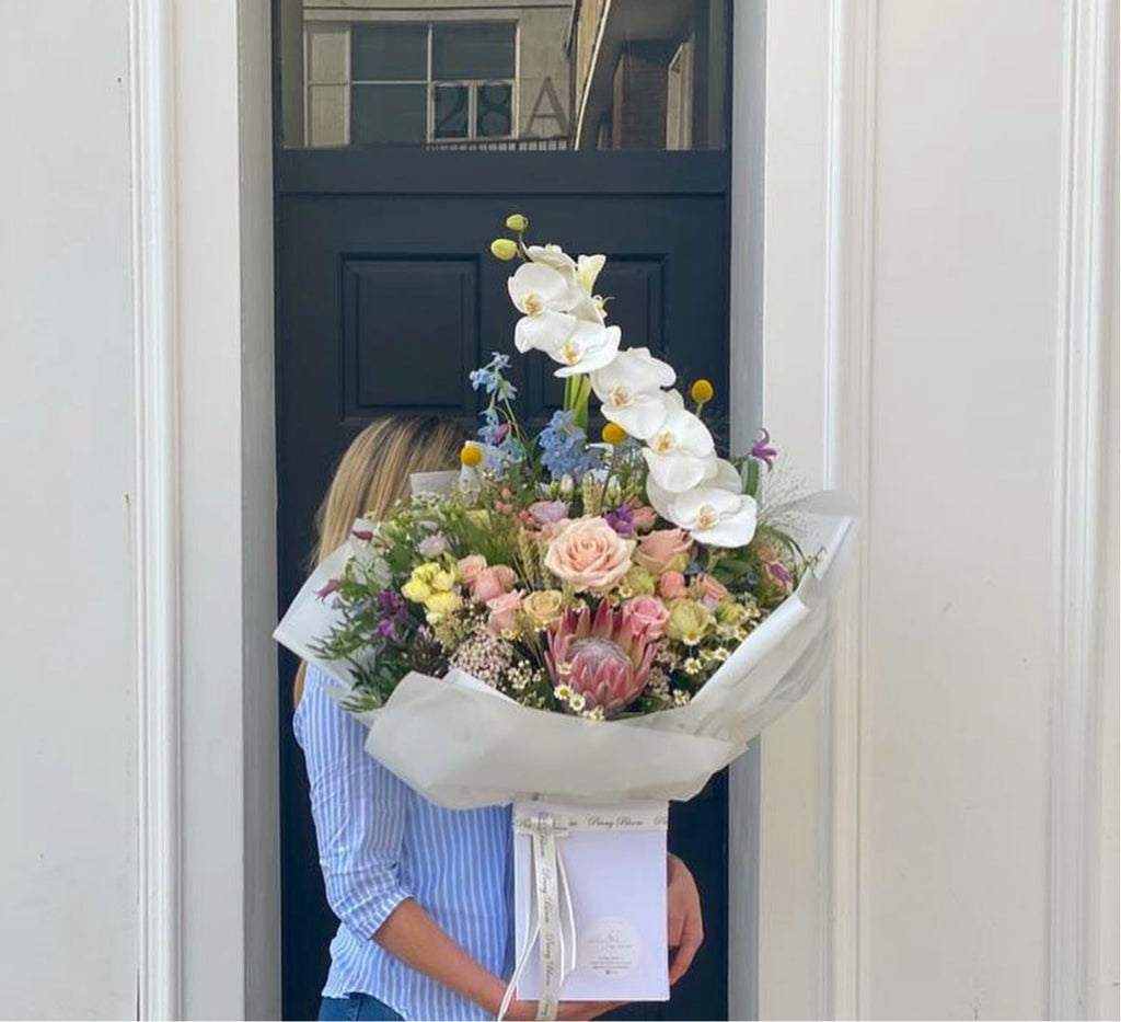 white bouquet with fresh spring flowers including orchids, bluebells, roses, protea, daisies, was flower and thistle.